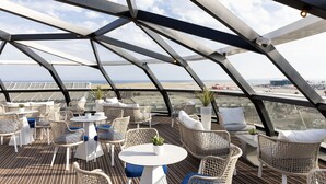 A rooftop lounge with wicker furniture, a white table, and a view of the airport.