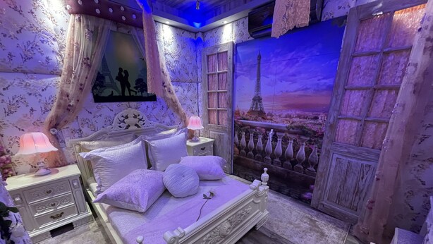 Ein Schlafzimmer mit einem Bett, Nachttischen, einer Lampe und einem Wandgemälde vom Eiffelturm.