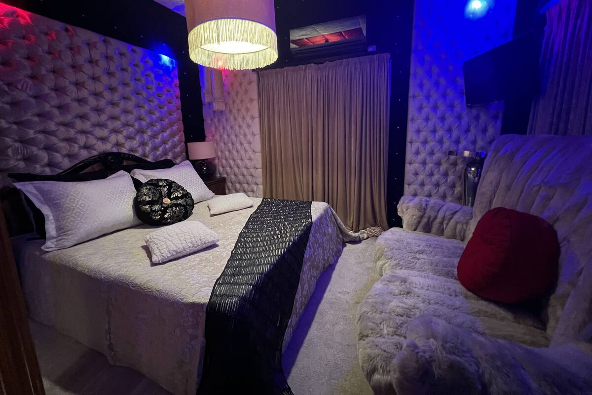 A luxurious bedroom with a tufted headboard, a large bed with multiple pillows, a fluffy white sofa, and a hanging light fixture.