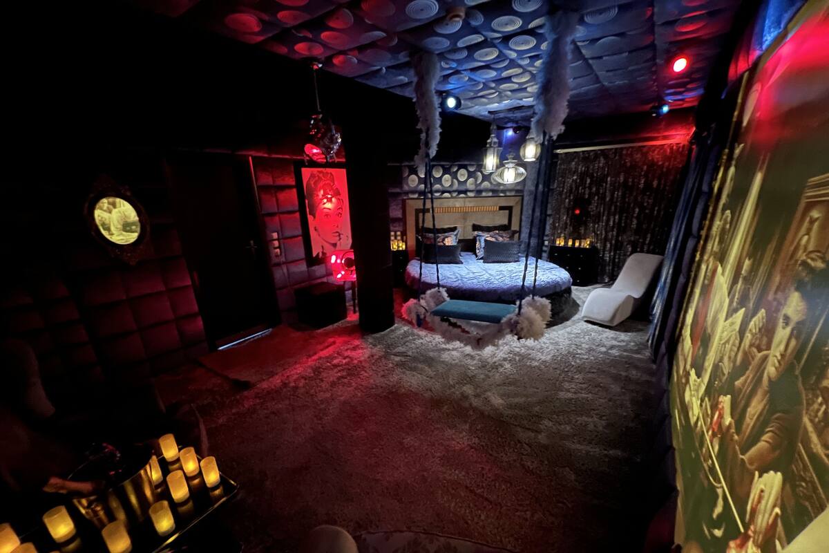 A dimly lit room with a bed, a swing, and a wall with a circular window.