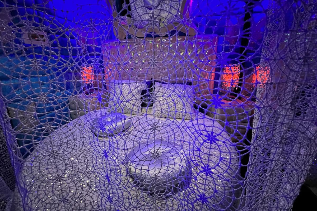 A room with a circular seating area, a bed, and a window with a view of the outside.
