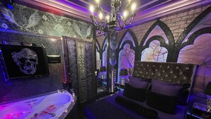 Ein luxuriöses Schlafzimmer mit einem großen Bett, einer Badewanne mit roten Verzierungen und Wanddekorationen im gotischen Stil.
