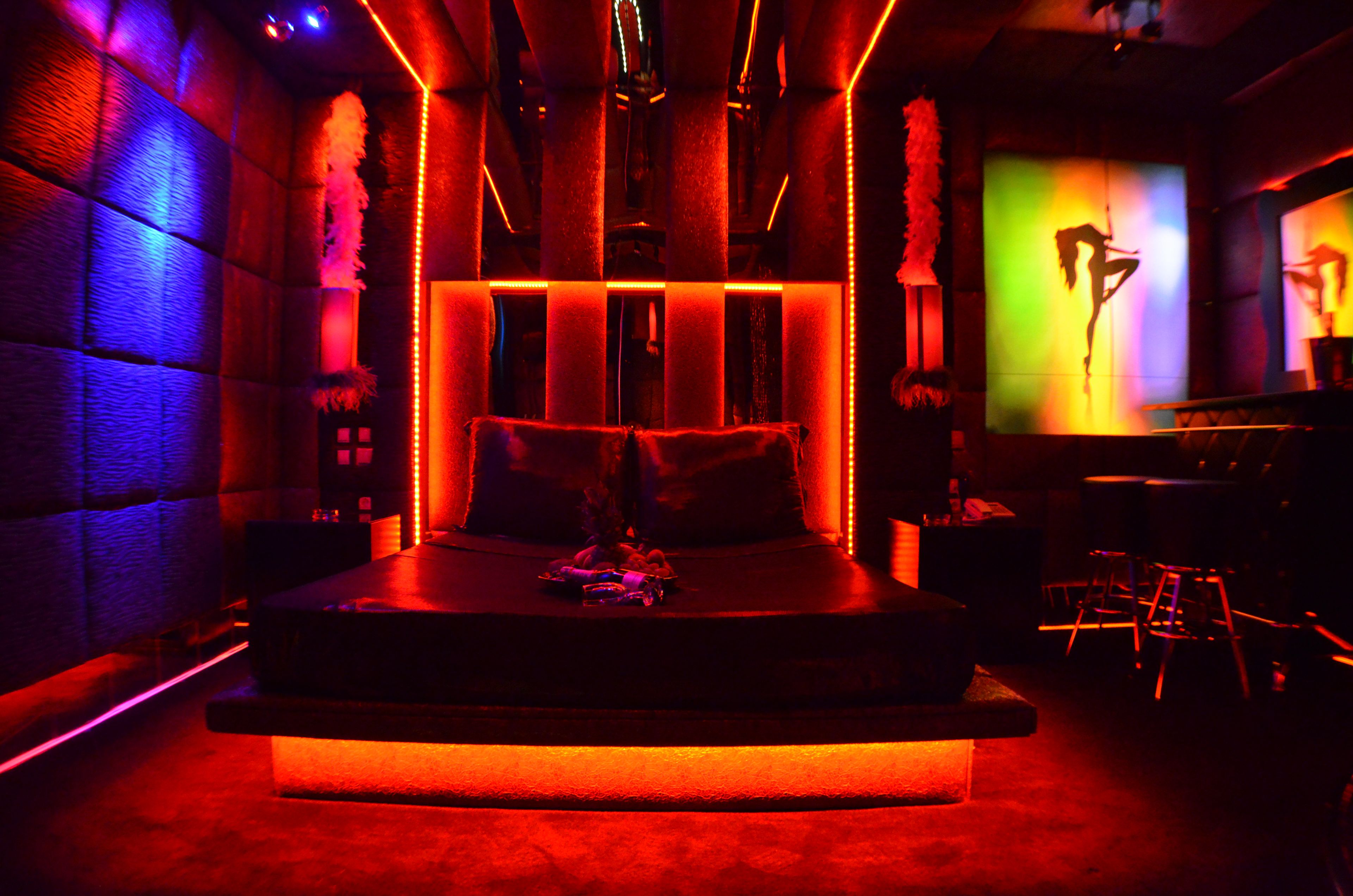 A dimly lit room with a bed, a bar area, and a screen displaying a silhouette.