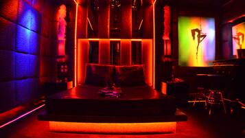 A dimly lit room with a bed, a bar area, and a screen displaying a silhouette.