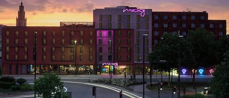 A hotel with a neon sign, a clock tower in the background, and a roundabout with traffic lights.