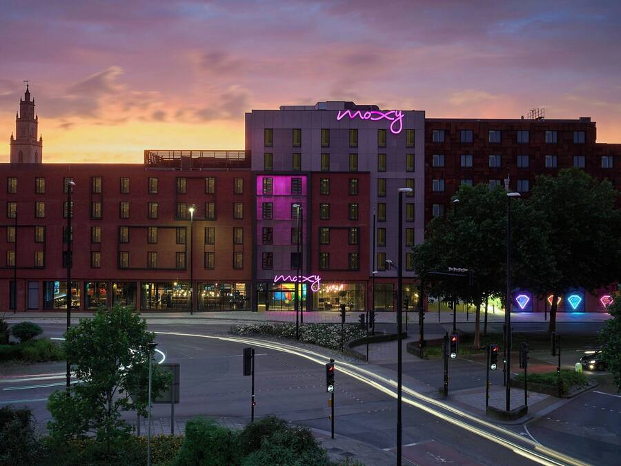 Ett hotell med en neonreklamskylt, ett klocktorn i bakgrunden och en rondell med trafikljus.