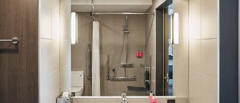 A modern bathroom with a large mirror, a shower, and a sink.