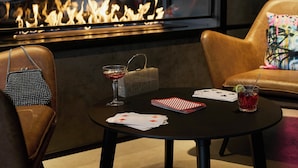 A cozy seating area with a leather couch, a small round table with playing cards and a drink, and a fireplace in the background. - Moxy Bristol (Bristol)
