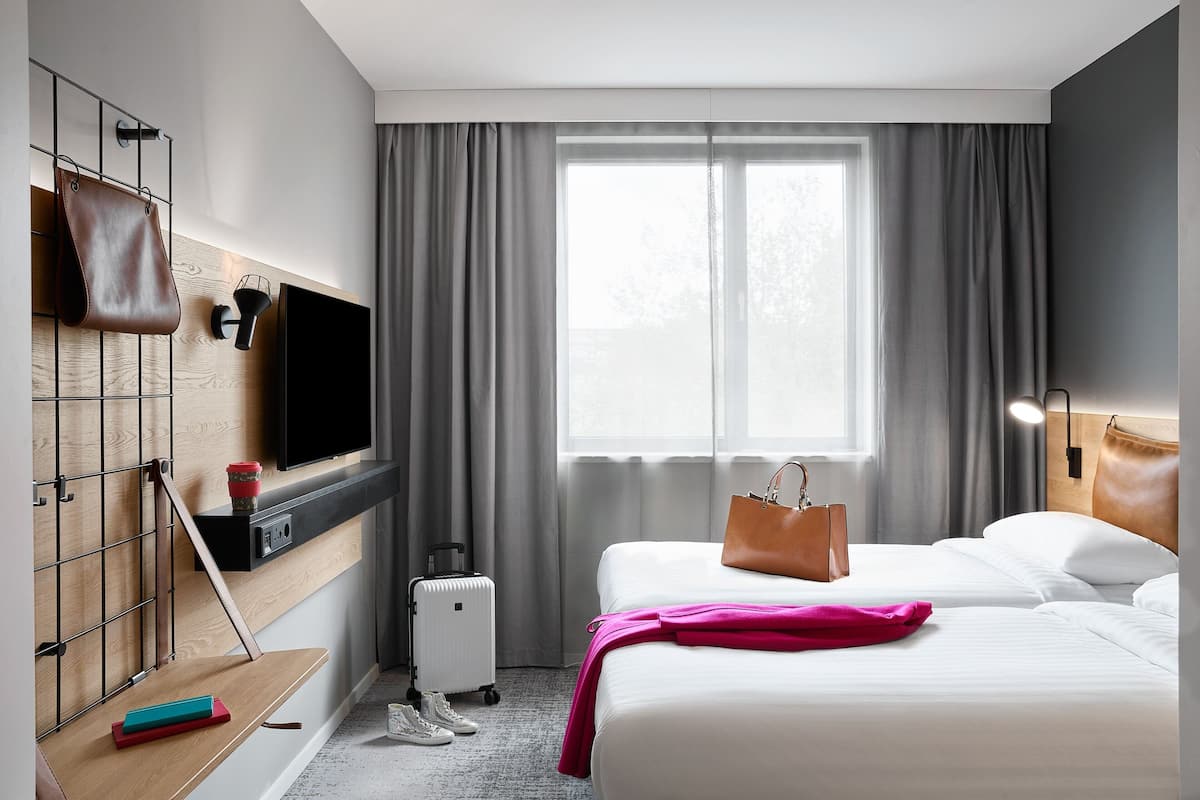A hotel room with a bed, a TV mounted on the wall, a suitcase, and a handbag on the bed.