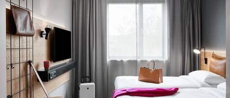 A hotel room with a bed, a TV mounted on the wall, a suitcase, and a handbag on the bed.