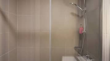 Ducha con puerta de vidrio, cabezal de ducha manual y una botella de champú rosa en la pared.