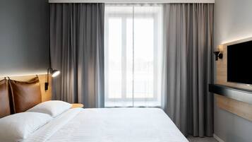 A hotel room with a large bed, a flat-screen TV mounted on the wall, and a window with curtains.