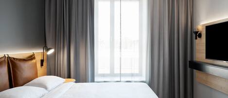Ein Hotelzimmer mit einem großen Bett, einem flachbildfernseher an der Wand und einem Fenster mit Vorhängen.