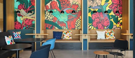 Ein stilvoller Lounge-Bereich mit Sitzgelegenheiten, Tischen und farbenfroher Wandgestaltung mit stilisierten Tierdarstellungen.