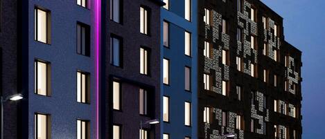 Un hotel moderno con un llamativo letrero de neón, varios pisos y una entrada bien iluminada.