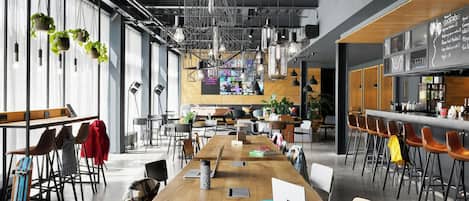A modern co-working space with long tables, chairs, and a bar area.
