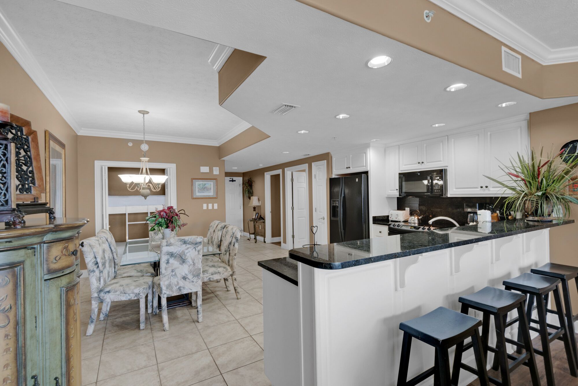 Una cocina amplia con gabinetes blancos, una isla central con taburetes de bar y un comedor con candelabro.
