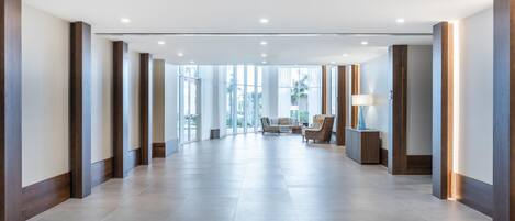A spacious hotel lobby with a modern design, featuring a long corridor, seating area, and large windows.