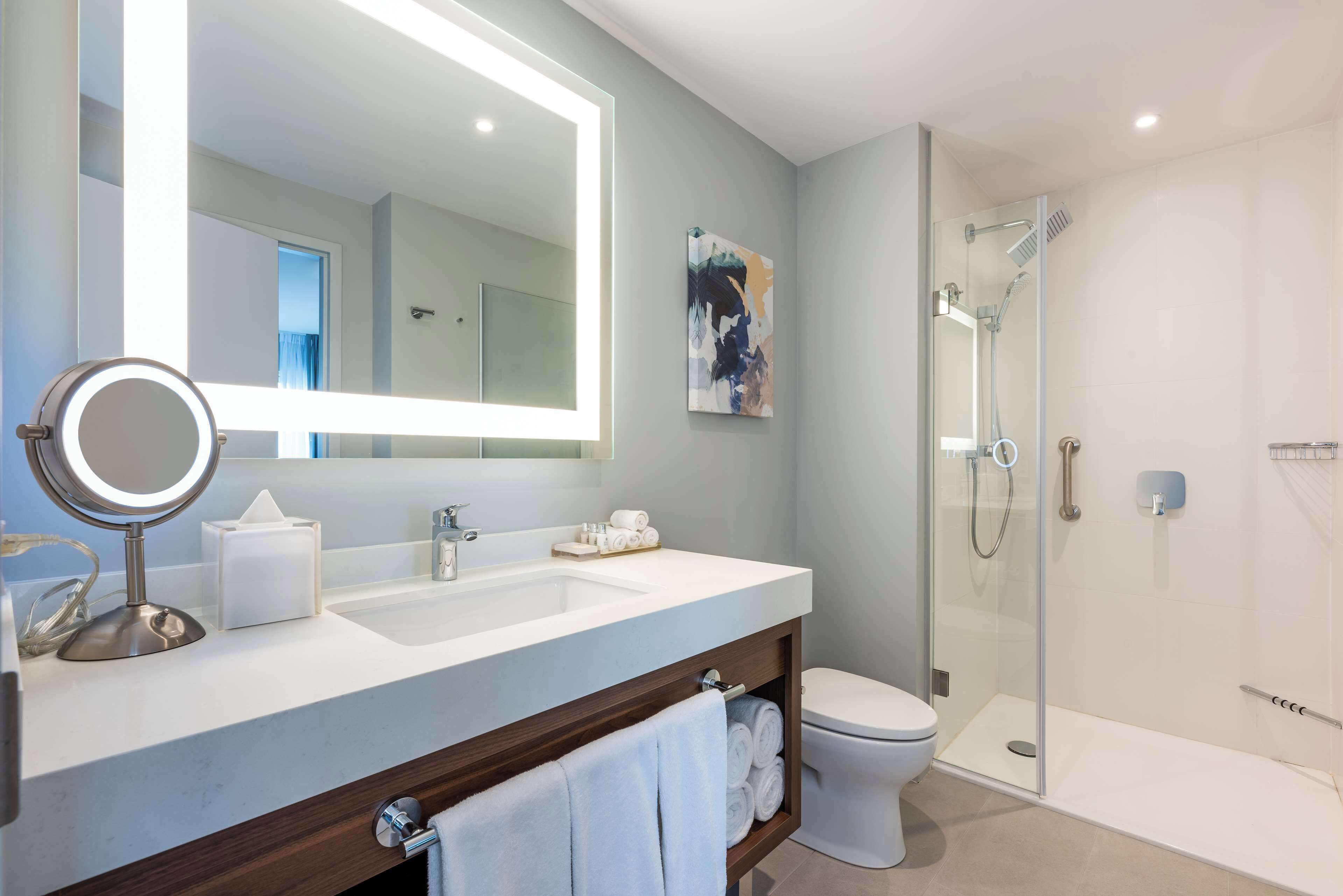 A modern bathroom with a large mirror, dual sinks, a glass shower enclosure, and a toilet.