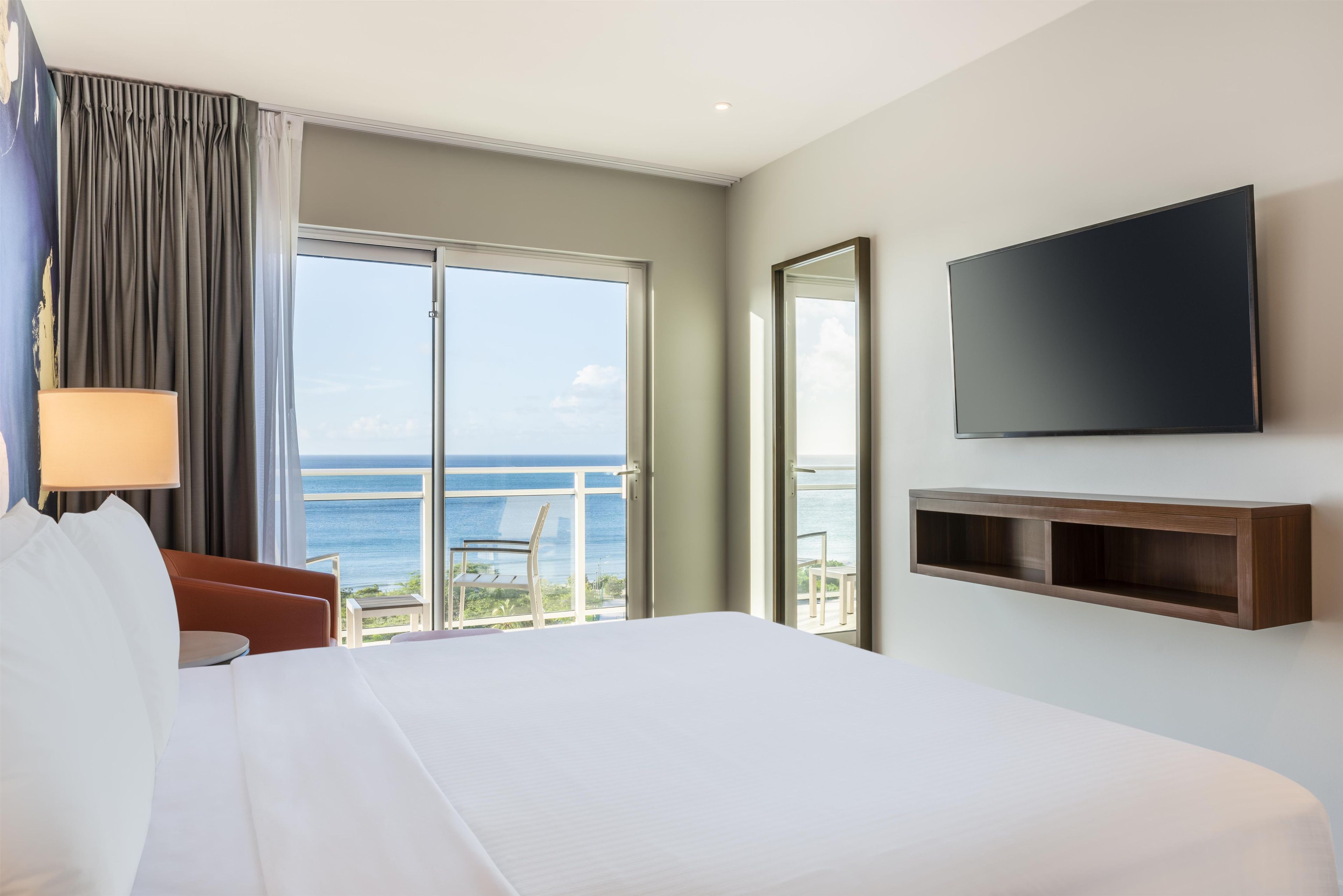 Una habitación de hotel con una cama grande, un televisor montado en la pared y vista al océano por la ventana.
