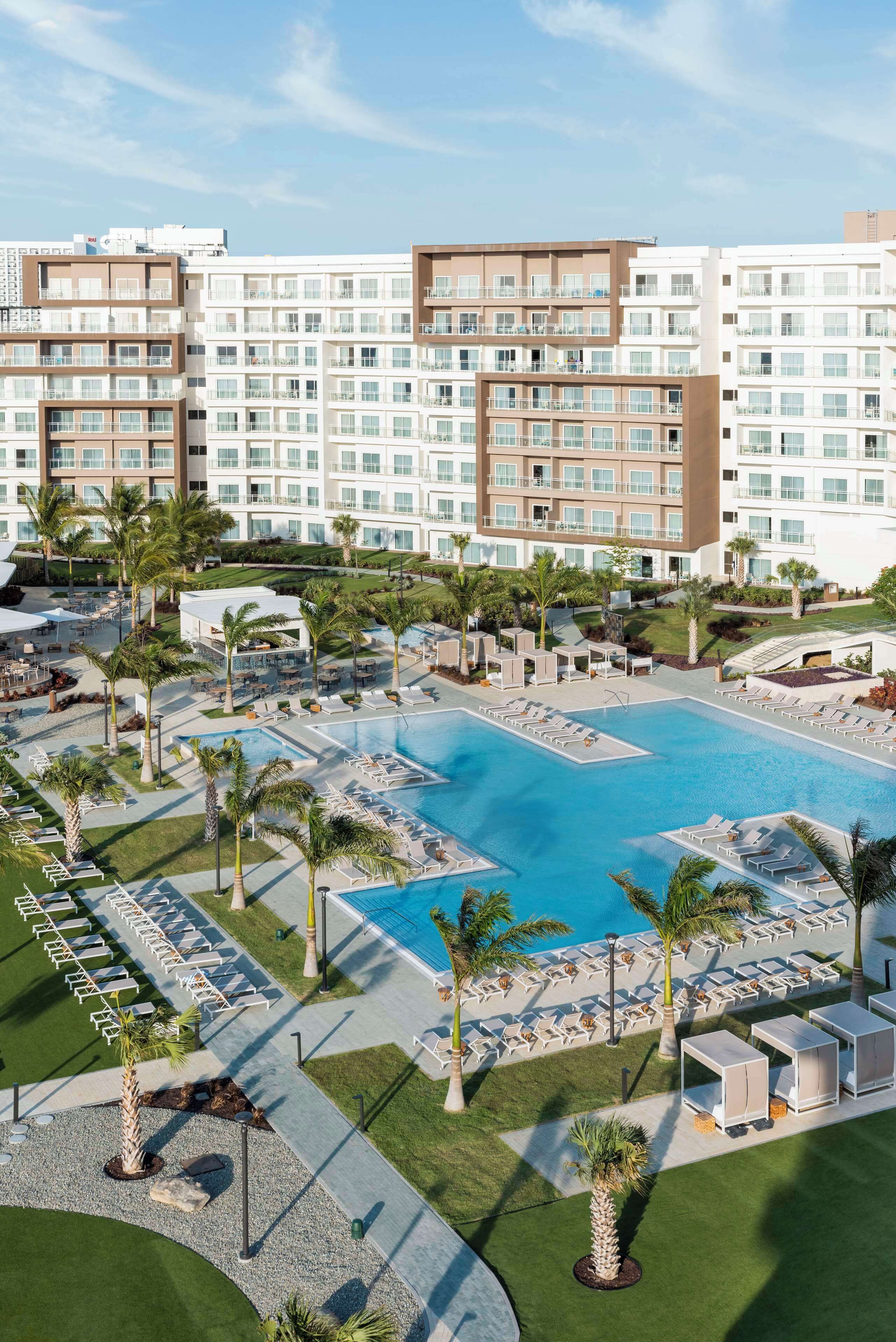 Ein Hotel mit einem großen Schwimmbecken, umgeben von Palmen und Liegestühlen.