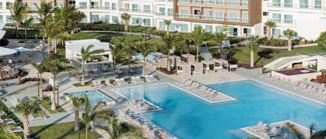 Un hotel con una gran piscina rodeada de palmeras y sillones de descanso.