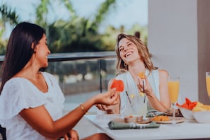 Two people sitting at an outdoor table with a glass of orange juice and various snacks. - Embassy Suites By Hilton Aruba Beach Resort (Noord)