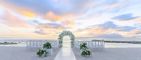 Decoración de boda en la playa con pasillo blanco, arco floral y sillas blancas.