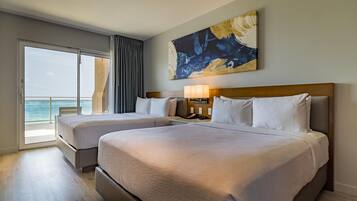 Habitación de hotel con dos camas, un ventanal con vistas, un cuadro en la pared y una mesita de noche con lámpara.