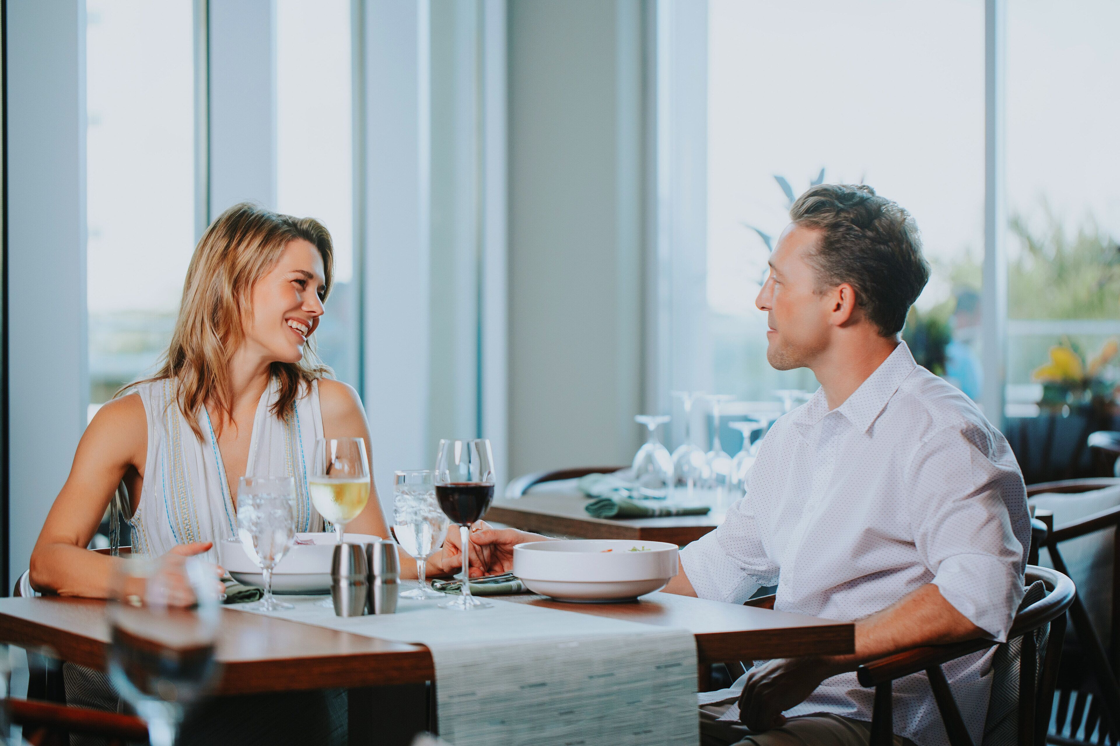 Una mesa de comedor con dos personas sentadas, una copa de vino y un tazón de comida.