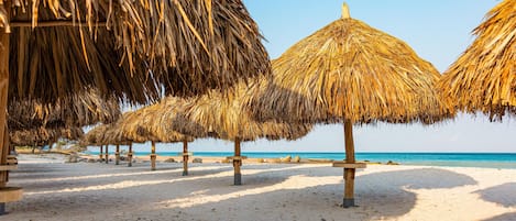 A beach with thatched umbrellas and a clear view of the ocean.