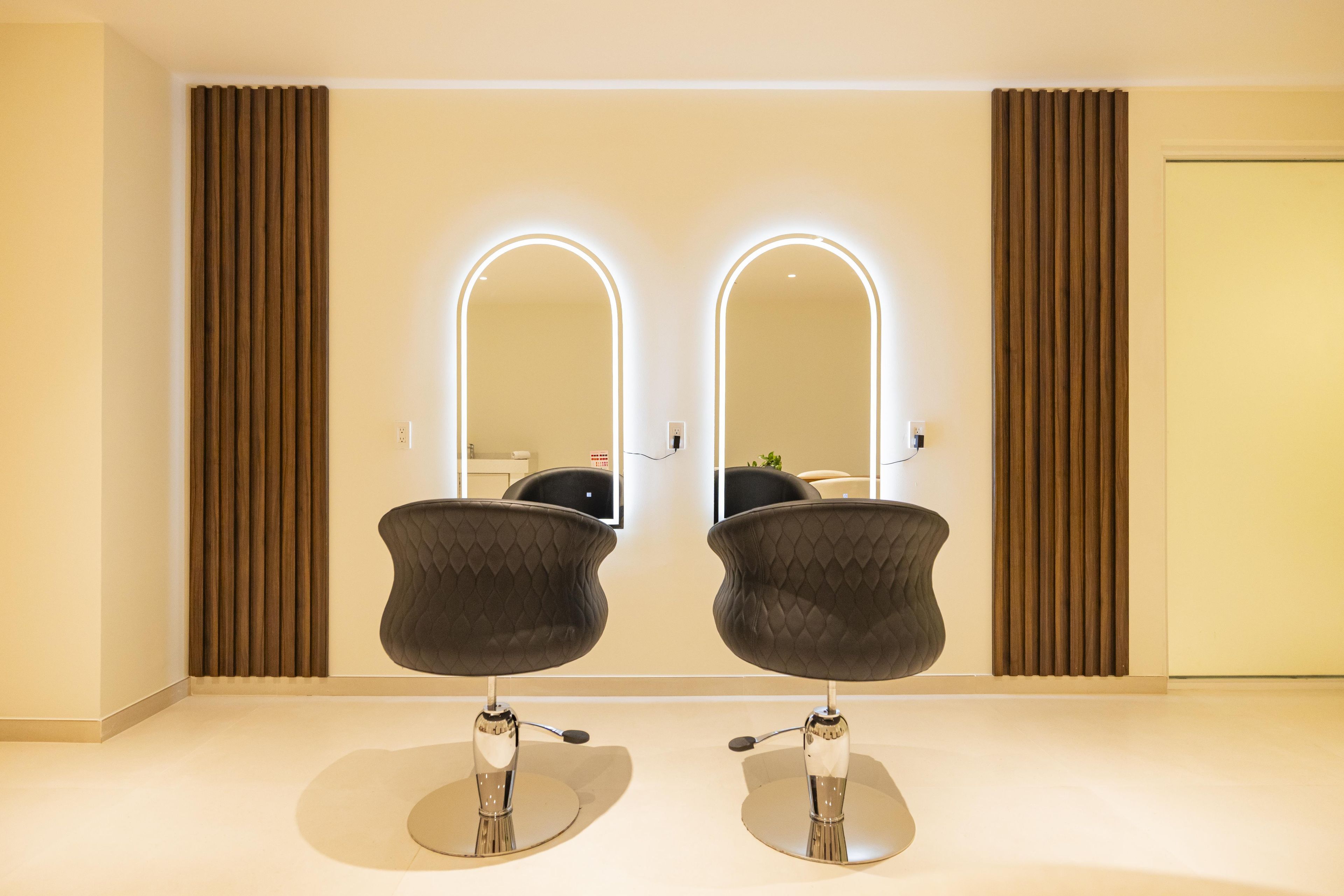 A room with two mirrored vanity mirrors, a black chair, and a door.