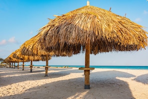 A beach with thatched umbrellas and wooden posts. - Embassy Suites By Hilton Aruba Beach Resort (Noord)