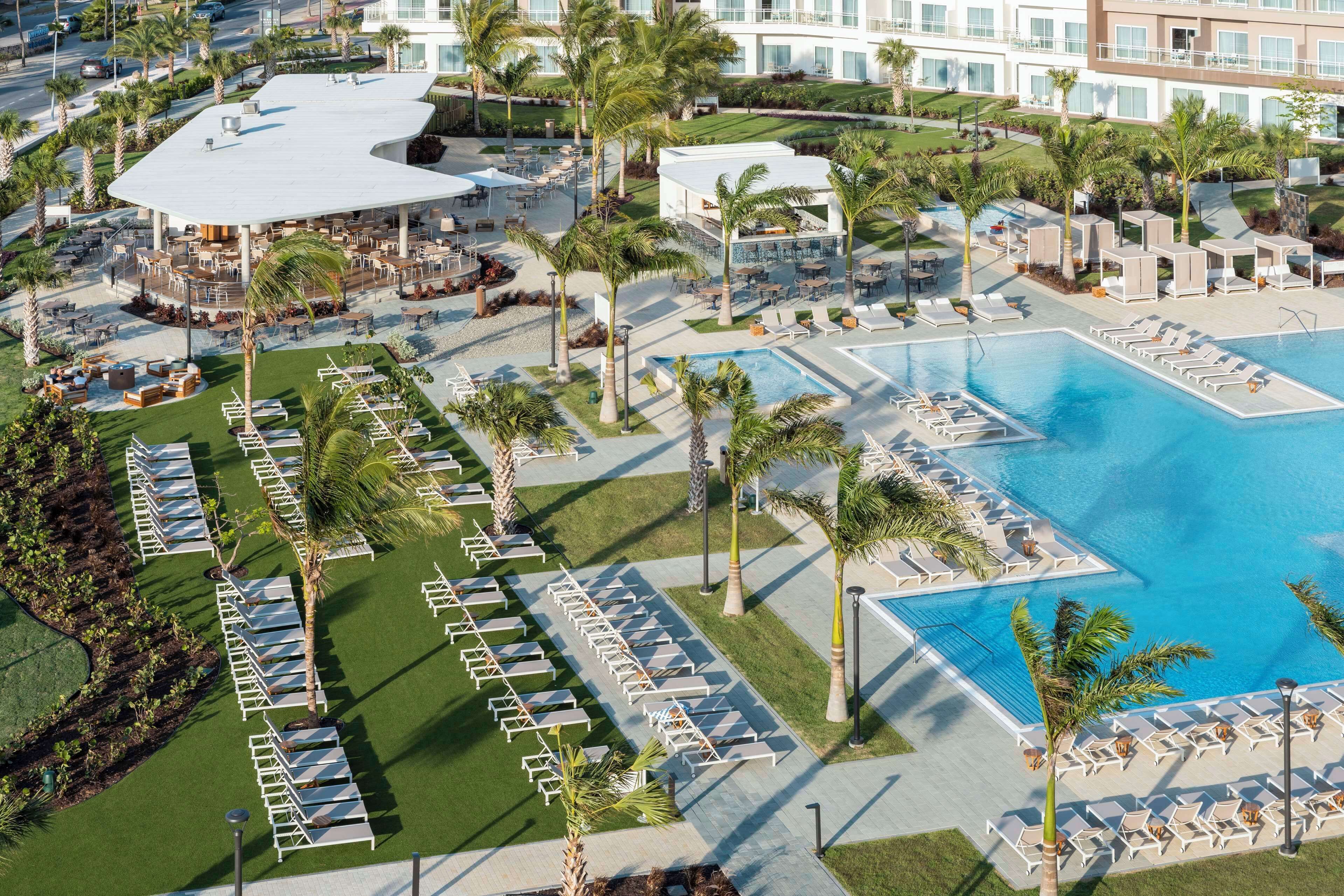 A resort with a large pool, sun loungers, and palm trees.
