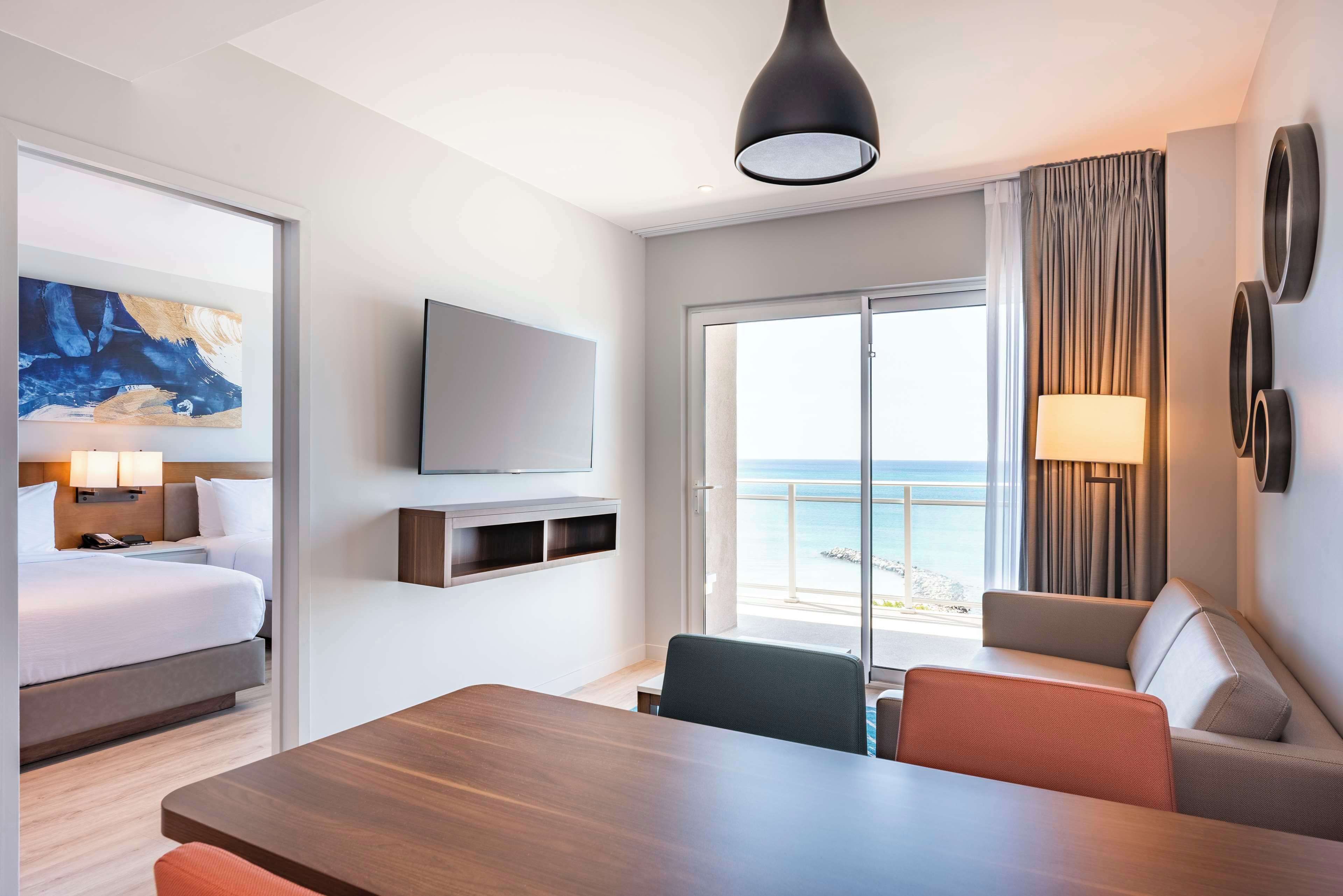 Habitación de hotel con cama, escritorio, televisor, sofá y balcón con vista al mar.