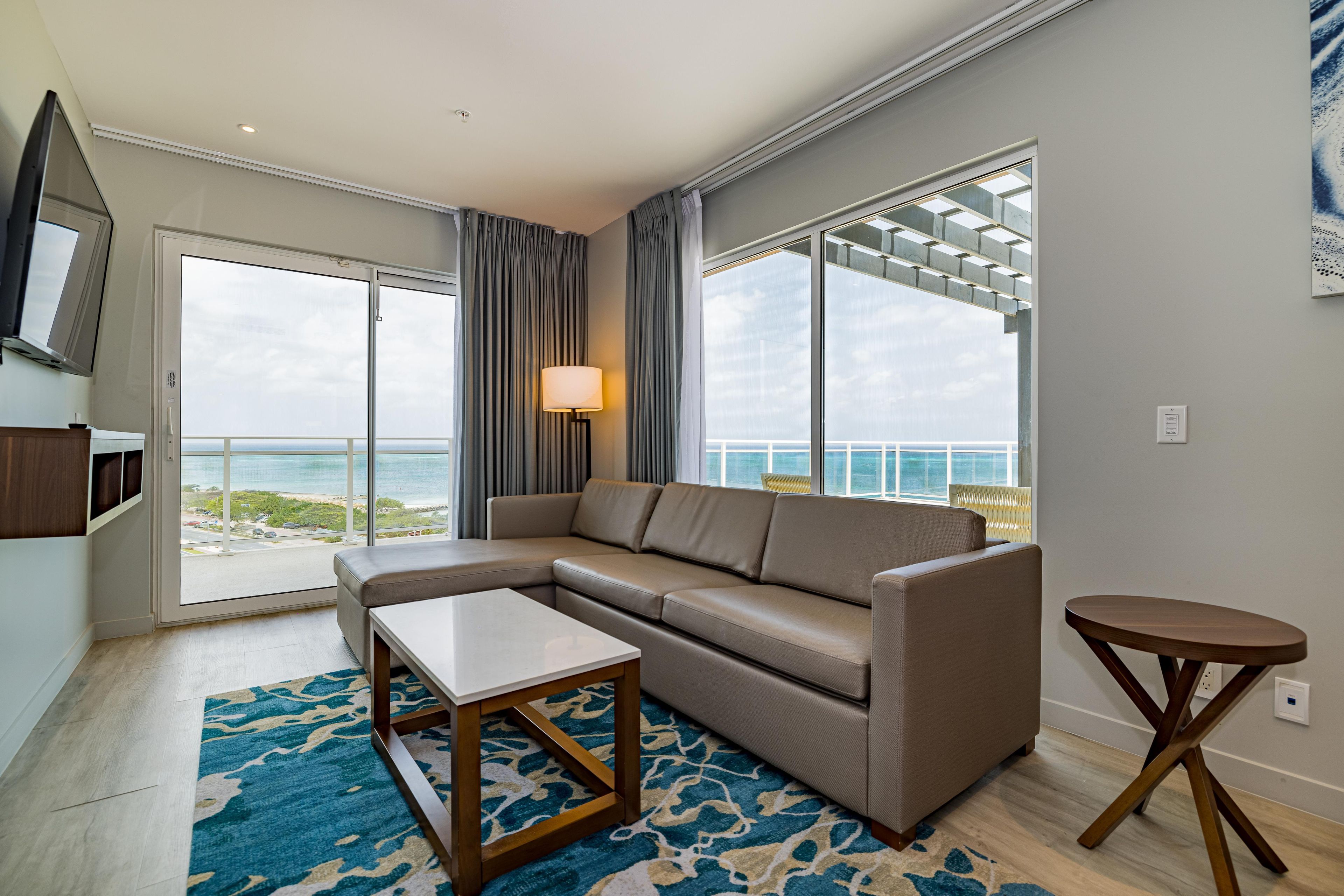 A modern living room with a sectional sofa, a small table, and a view of the ocean through large windows.
