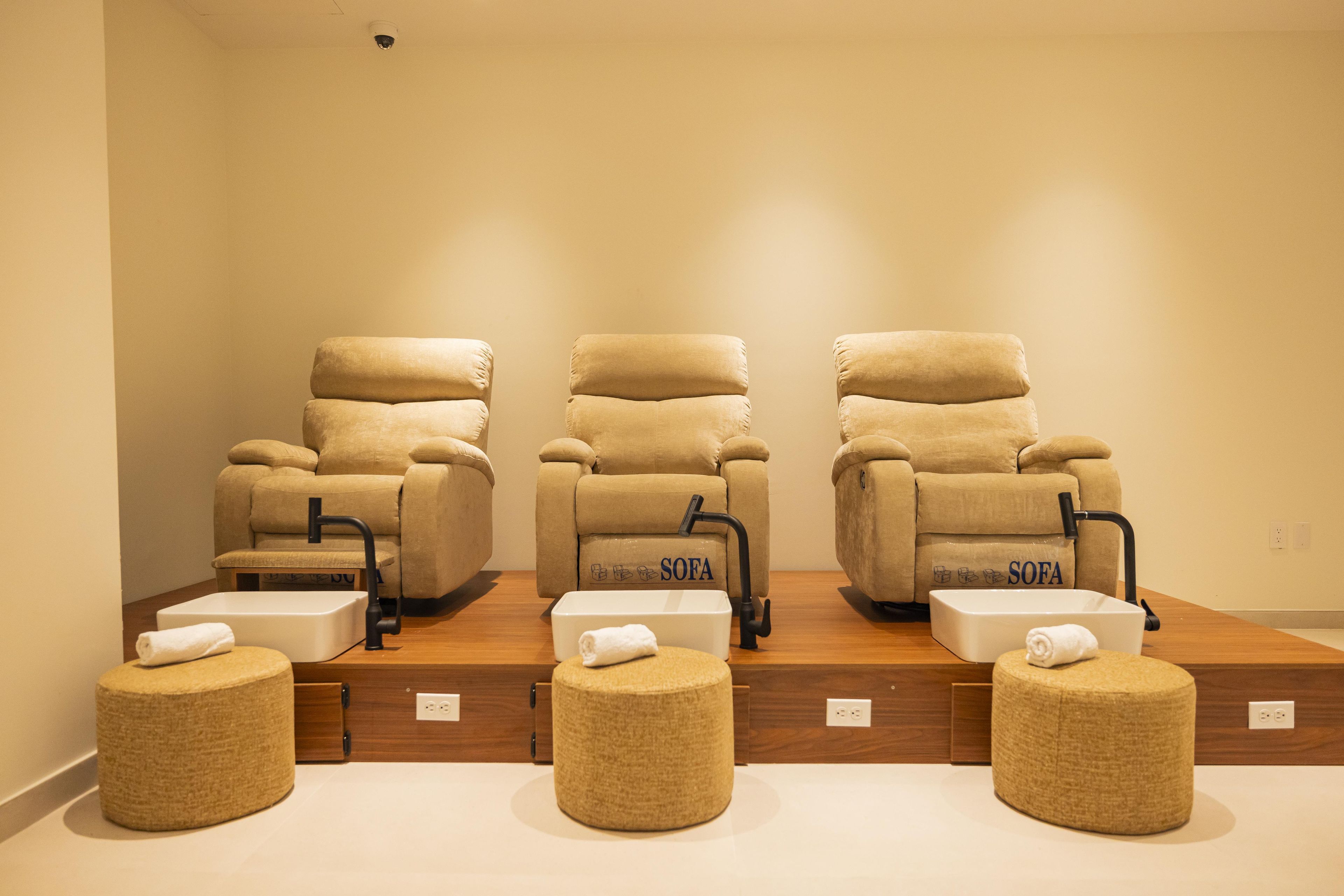 A spa room with three SOFA massage chairs, a foot bath, and a wooden floor.