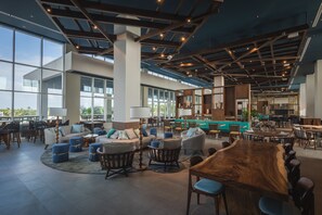 A spacious lounge area with a large wooden table, comfortable seating, and large windows offering views of the outdoors. - Embassy Suites By Hilton Aruba Beach Resort (Noord)