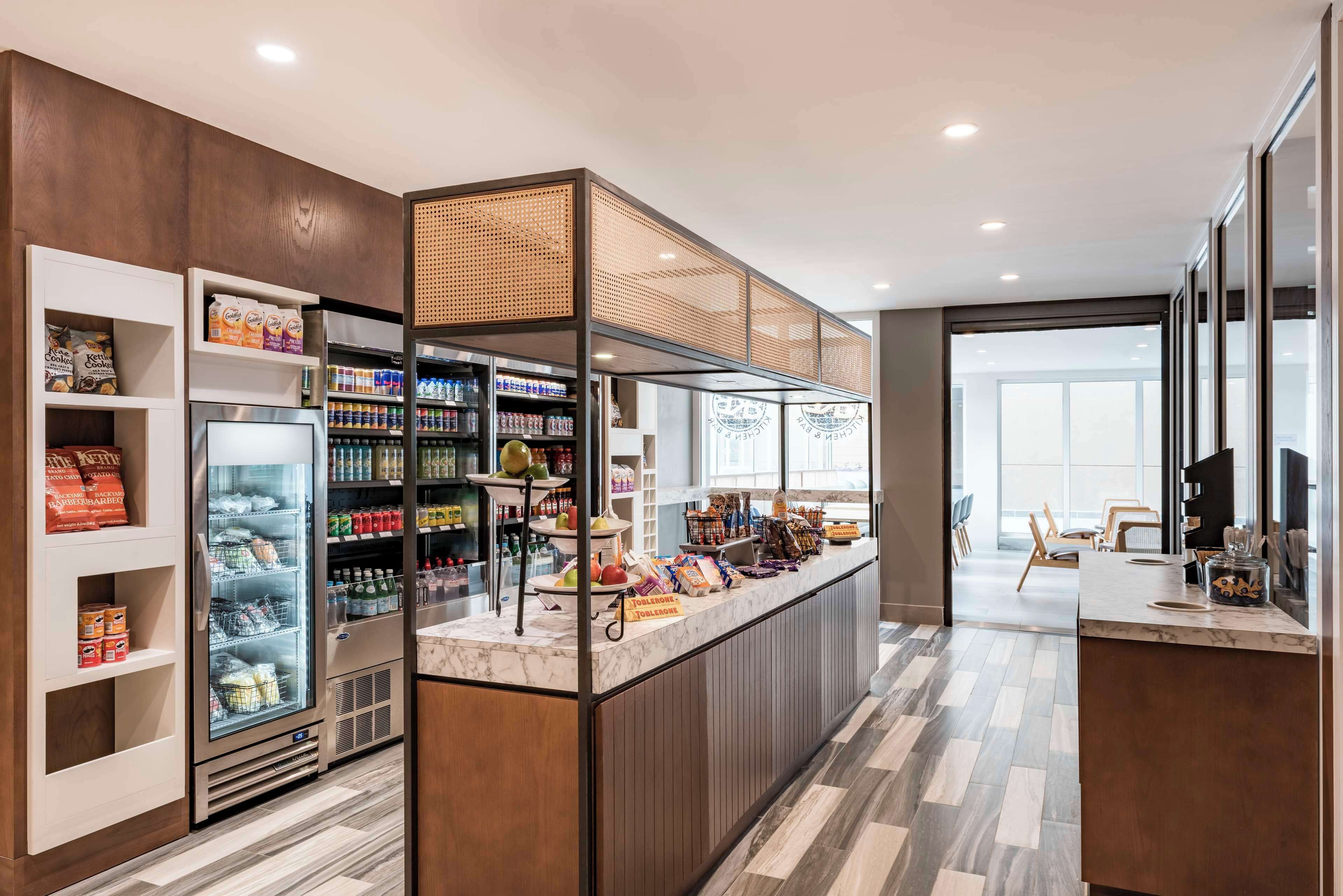 A modern cafe with a marble counter, refrigerated display, shelves stocked with snacks, and a view of the outside.