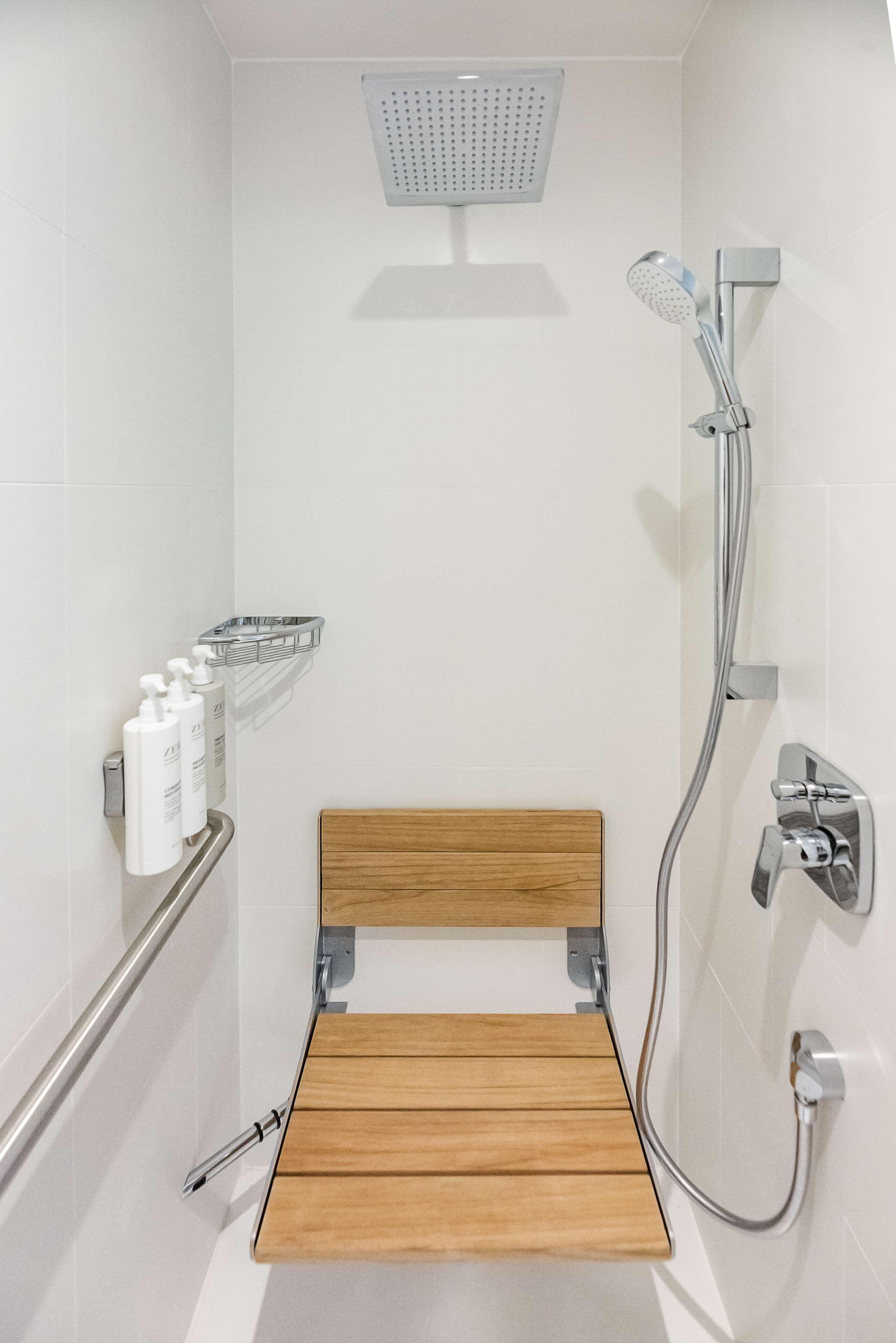A shower with a handheld showerhead, a wooden bench, and a metal shelf with toiletries.
