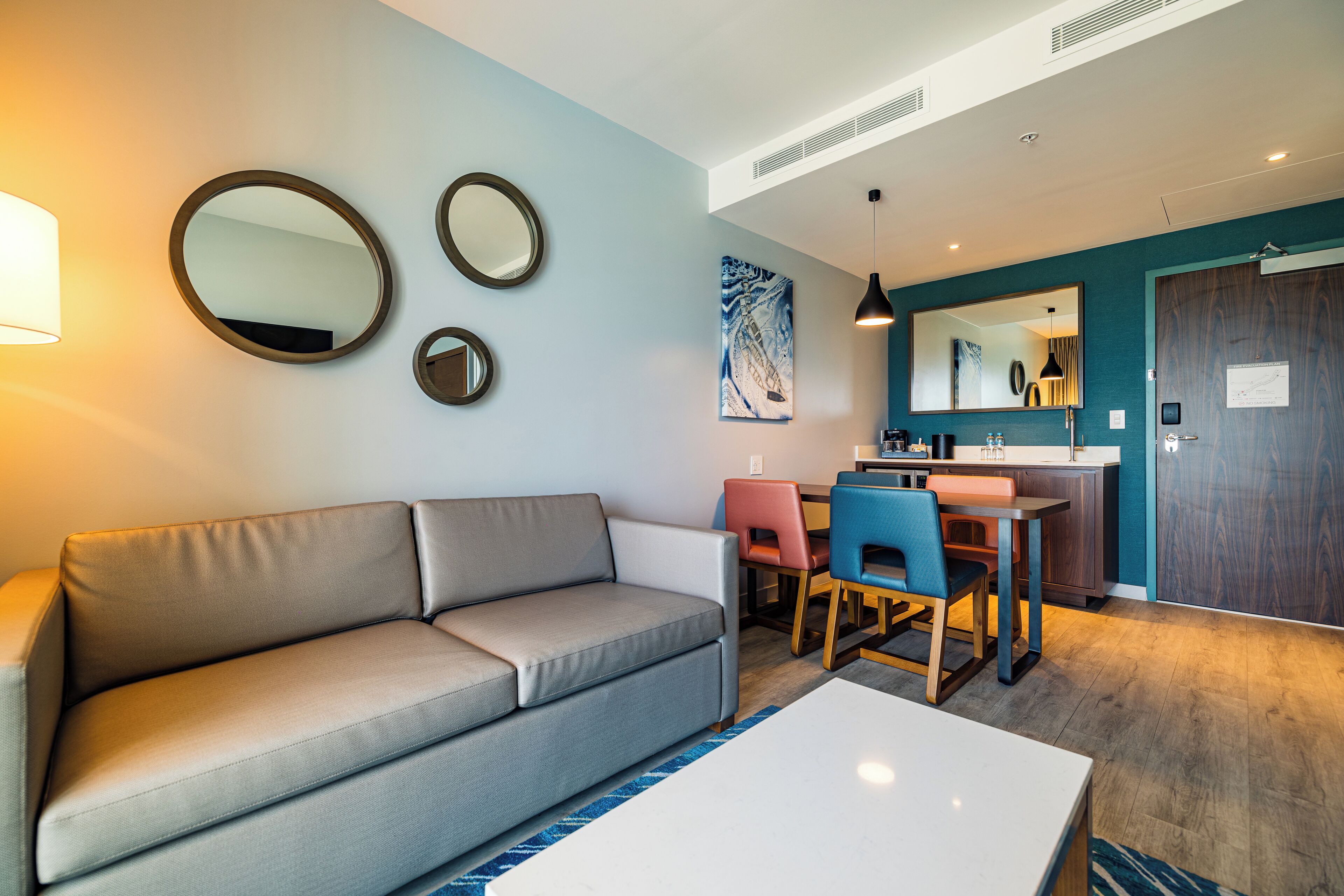 A modern living room with a sofa, a dining table with chairs, and a kitchen area in the background.