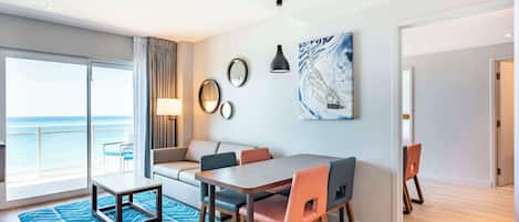 A modern hotel room with a balcony, a dining area, and a large window offering a view of the sea.