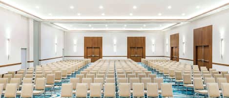 Un amplio salón de conferencias con filas de sillas, puertas de madera y una alfombra azul estampada.