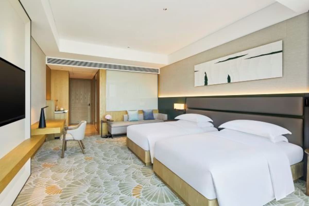 A hotel room with two beds, a TV, a desk, and a seating area.
