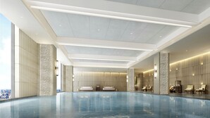 Una piscina interior moderna con zonas de descanso, ventanas amplias y vista a la ciudad.