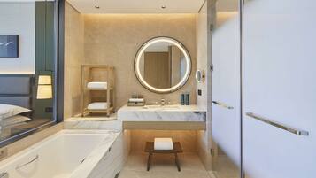 A modern bathroom with a large bathtub, a round mirror with a light, and a small stool.
