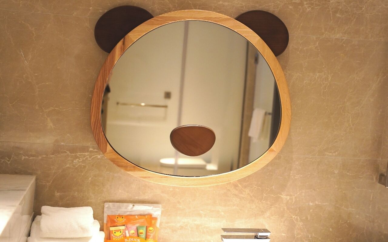 Un bagno con uno specchio tondo incorniciato in legno, un asciugamano e una piccola confezione sul ripiano.