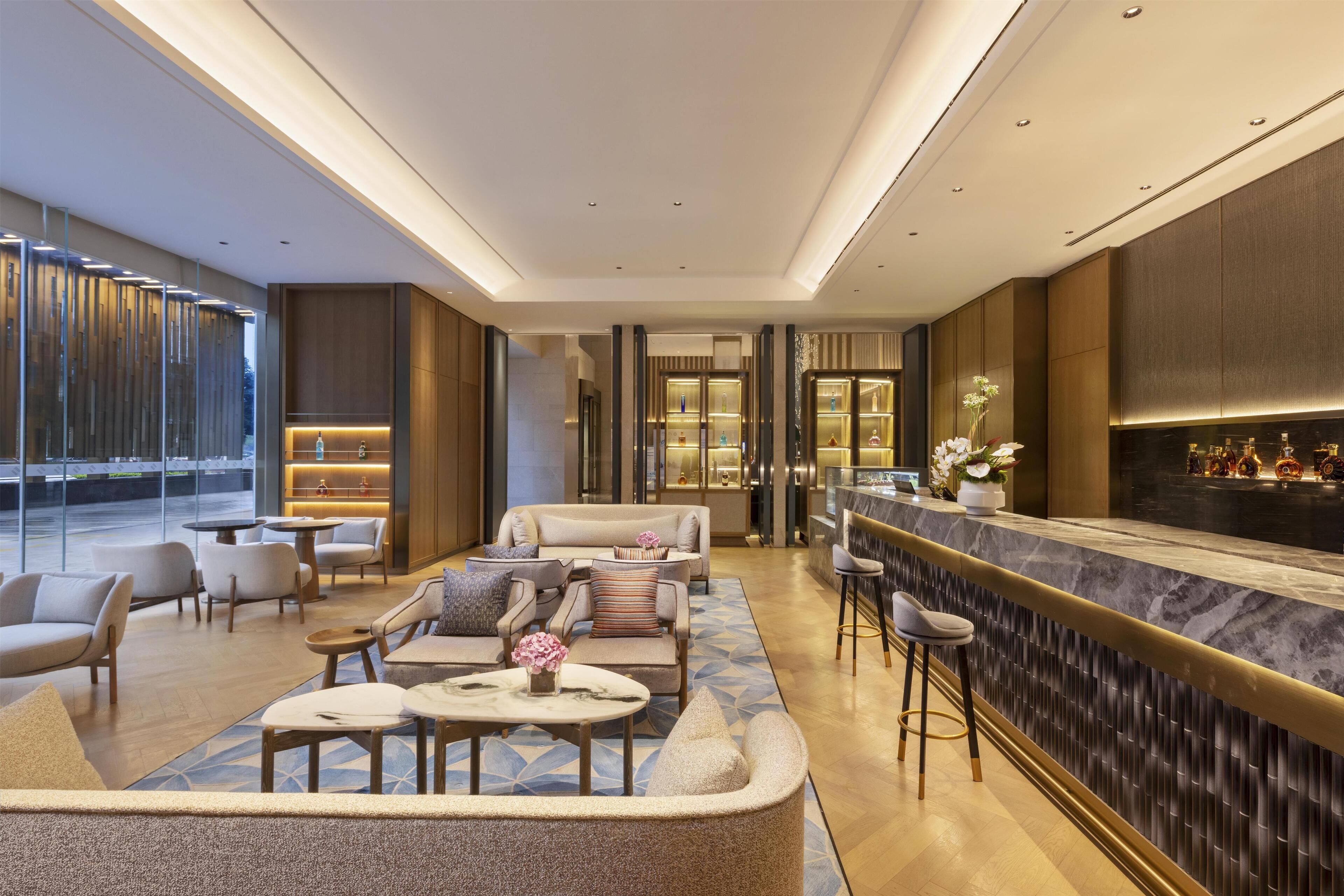 A modern hotel lobby with a bar area, seating arrangements, and a view of the outdoors.