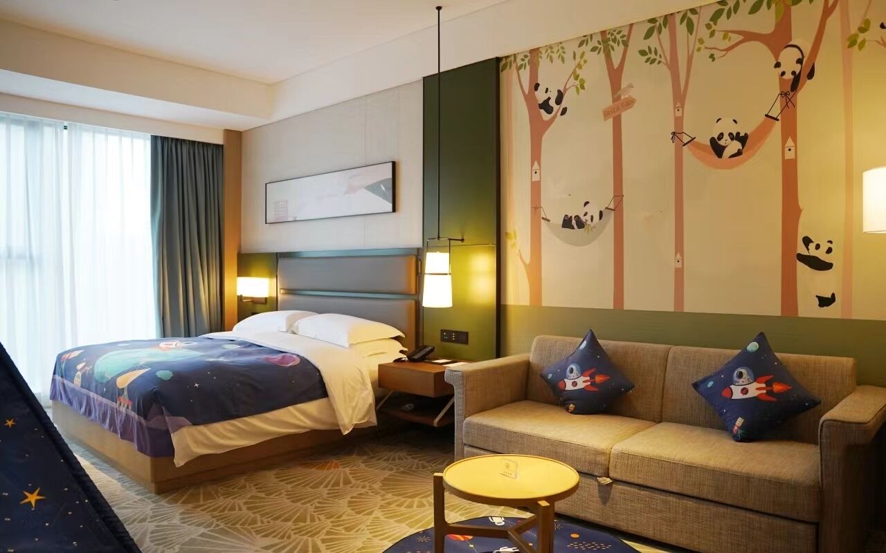 Habitación de hotel con cama, sofá, una mesita y un mural de un árbol en la pared.