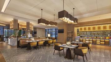 A modern hotel lobby with a bar area, seating arrangements, and a large window providing a view of the cityscape.